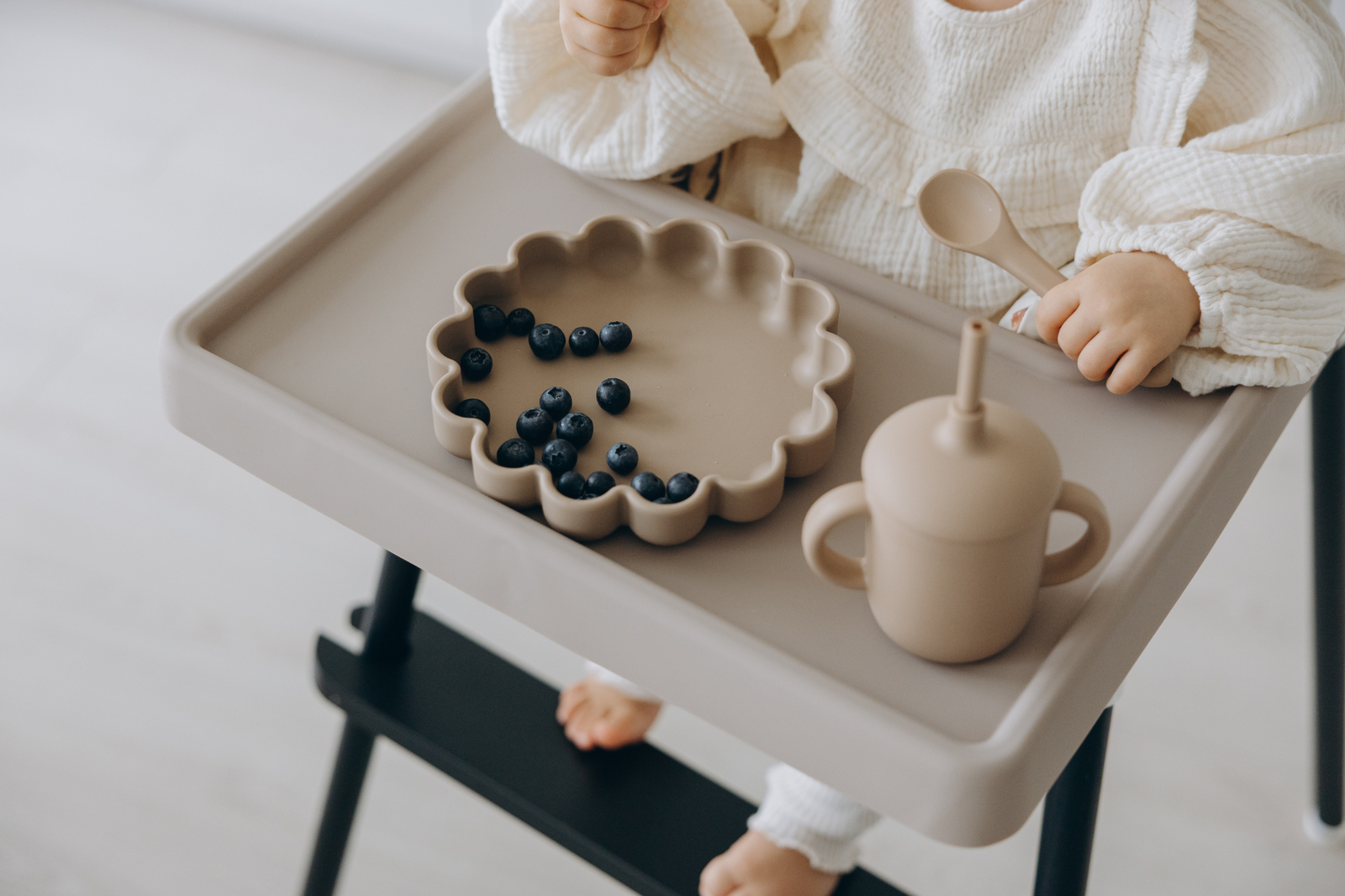 Baby using weaning essentials in IKEA highchair – scalloped silicone suction plate, sippy cup and spoon on taupe silicone placemat by azebabyDREAm 
