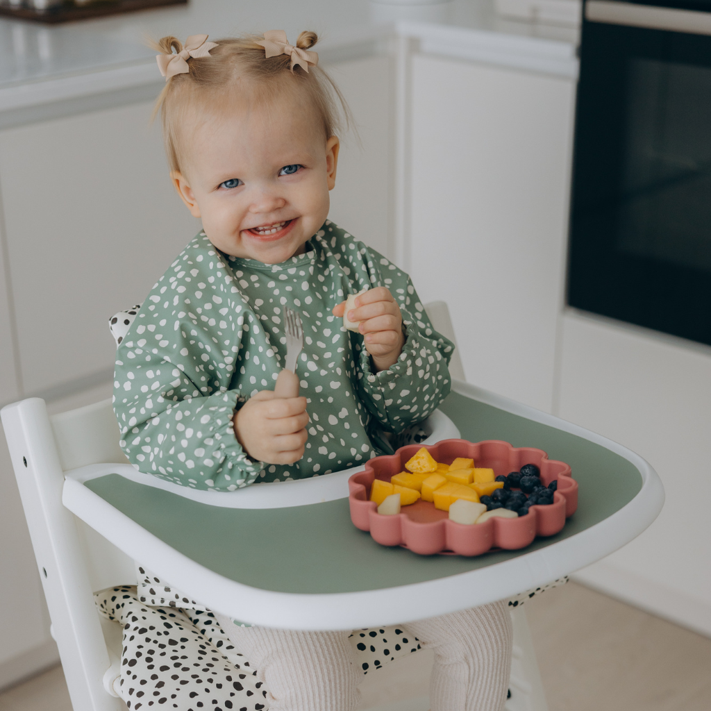 Smiling baby sitting on high strokke clasic highchair footrest