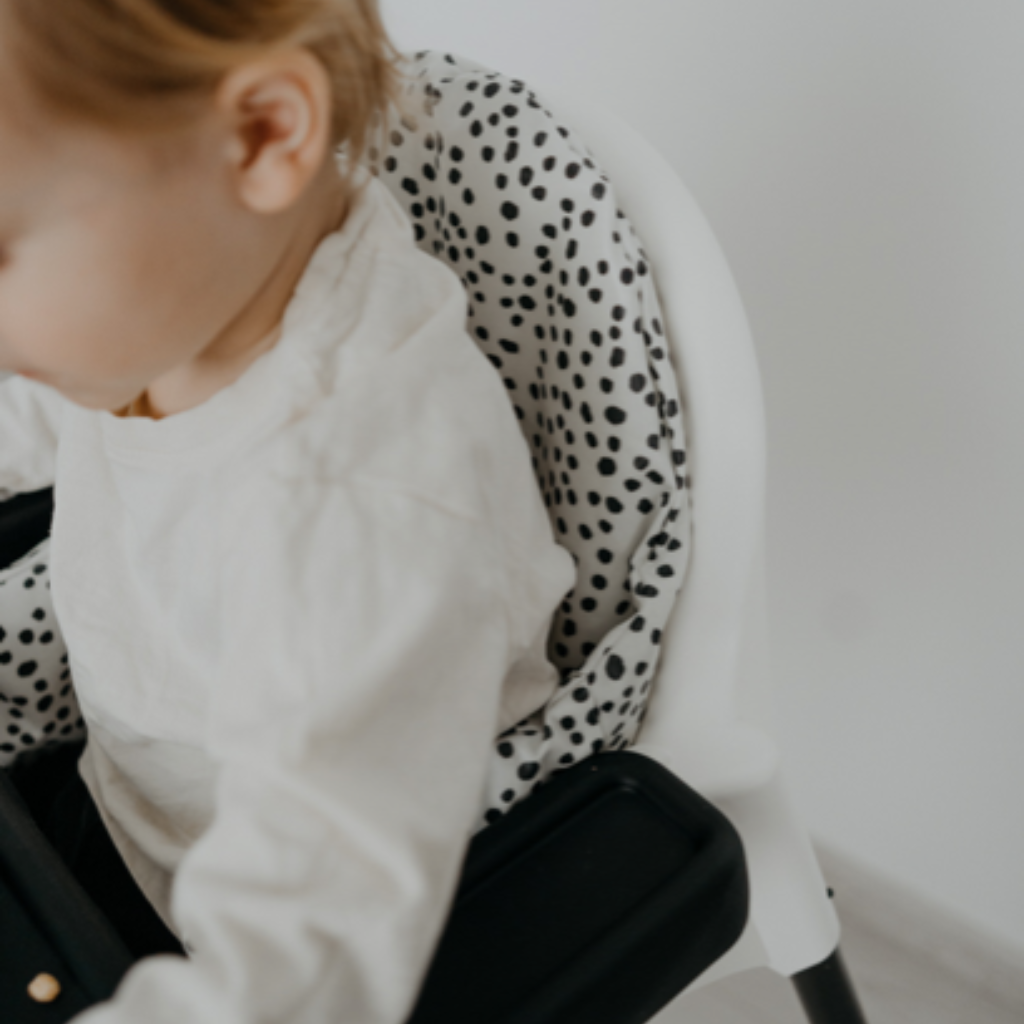 Side photo of baby sit on the chair white cushion with black dots 