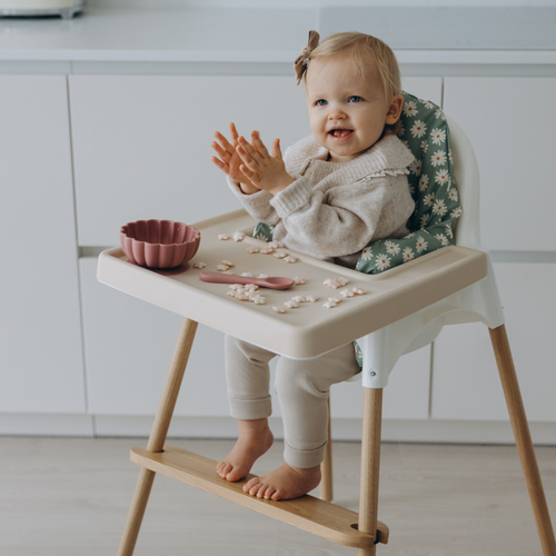 Baby seated in IKEA Antilop highchair with cream silicone placemat, wipe-clean cushion and natural oak leg wrpas by AZEbabydream