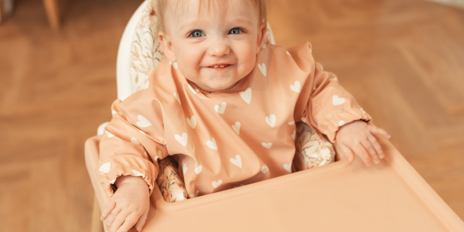 Baby eating in IKEA highchairs in wipe clean long sleeve bib in hearts on paech print  by AZEbabydream