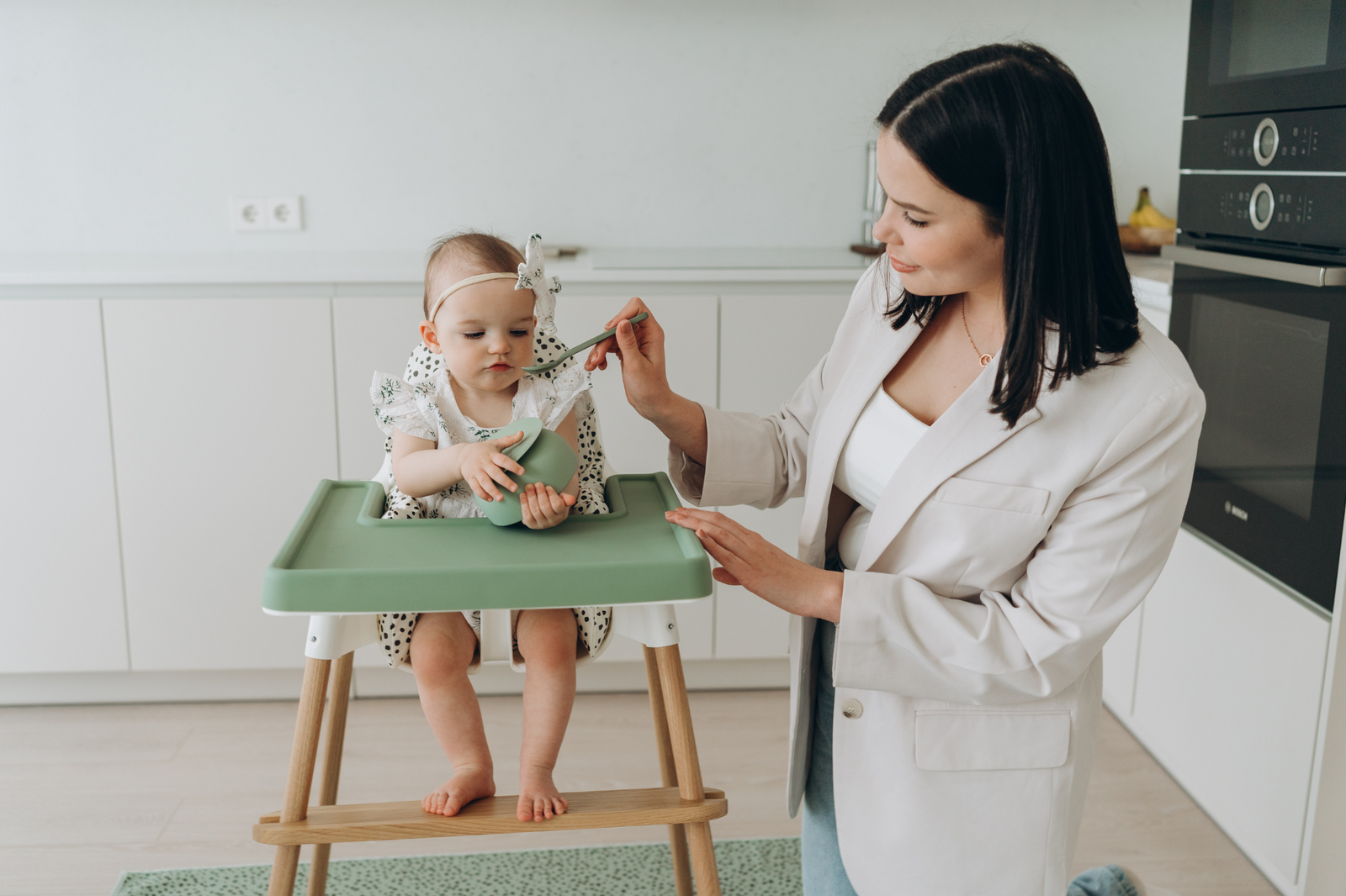 mum feeding baby in IKEA Antilop highchair with AZEbabydream green silicone placemat, matching suction bowl and weaning spoon