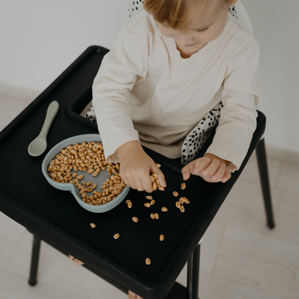 Background image of baby sitting on the black chair and playing with foods